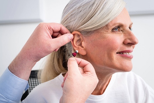 Ältere Frau bekommt modernes Hörgerät eingesetzt, Hörakustiker Beratung Hörhilfe Alltag.